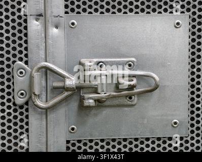 Metallverriegelung verschlossen, in industrieller Tür, mit Metallverriegelung, perforiertem Metallblech, aus einer Nahaufnahme-Perspektive, mit grauen, silbernen Akzenten und sichern a Stockfoto