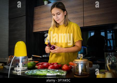 Junge Frau hackt frisches Gemüse auf einer Küchentheke, während sie eine gesunde hausgemachte Mahlzeit zubereitet. Hauskochen, ausgewogene Ernährung, frische Zutaten und Stockfoto