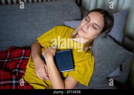 Müder Student ist mit einem Lehrbuch eingeschlafen, während er für Prüfungen lernte. Buchliebhaberin ist nachts mit einem Buch in den Armen eingeschlafen. Stockfoto