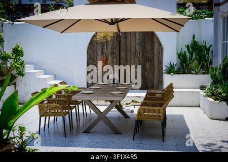 Ein Außenessbereich mit einem für acht Personen gedecktem Tisch unter einem Sonnenschirm. Stockfoto