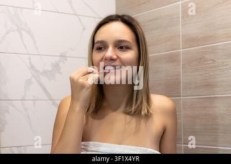 Frau, die Lippenbalsam oder Lippenstift auf ihre Lippen in einem gefliesten Badezimmer zu Hause aufträgt. Tägliche Schönheitsroutine, Lippenpflege und persönliche Kosmetik. Stockfoto