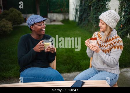 Verschiedene weibliche Freunde genießen heiße Getränke im Freien und lachen Stockfoto