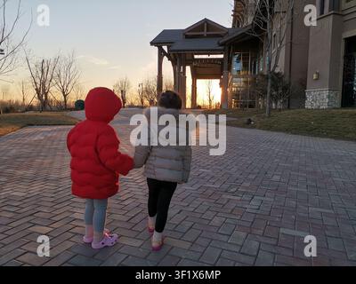 Zwei Kinder gehen Hand in Hand auf einem Ziegelweg während des Sonnenuntergangs. Stockfoto