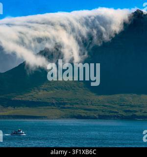 Dramatische tiefe Wolke, die über einen Bergrücken neben einem isländischen Fjord fließt Stockfoto