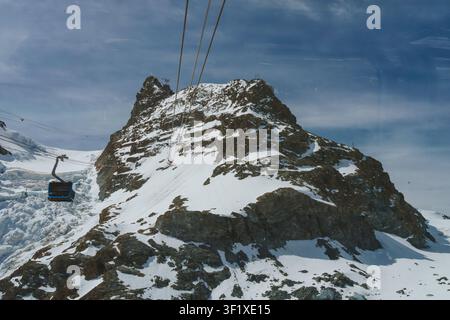 Seilbahn in Zermatt steigt einen schneebedeckten Berg hinauf, mit sichtbarem Gletscher Stockfoto