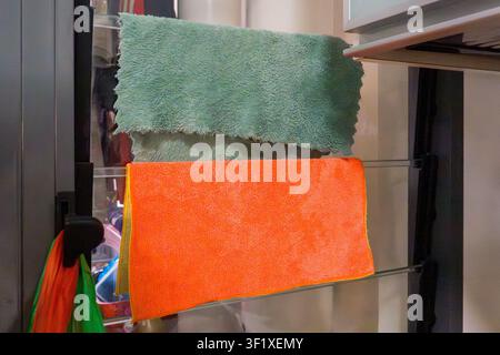 Zwei farbenfrohe Putztücher hängen an einem Glastürgriff. Eines ist grün, das andere leuchtend orange. Sie wirken weich und saugfähig, geeignet für die Reinigung Stockfoto