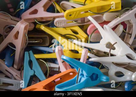 Hellfarbene Plastik-Waschklammern, die aufeinandergestapelt sind. Verschiedene Farbtöne, darunter Blau, Gelb, Rosa und Orange. Ein wirrer Haufen erzeugt eine lässige, unordentliche Atmosphäre Stockfoto