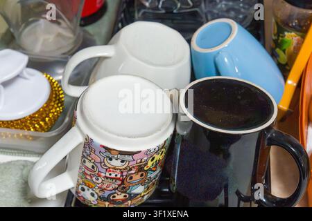 Vier Tassen stehen eng beieinander auf einer Oberfläche. Eine enthält eine dunkle Flüssigkeit, wahrscheinlich Kaffee oder Tee. Eine andere hat bunte Cartoonfiguren darauf gedruckt. Die dritte m Stockfoto
