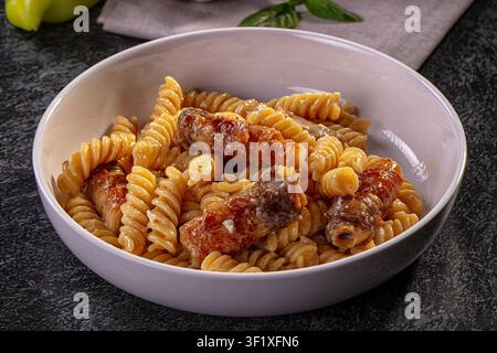 Nahaufnahme von Fusilli-Pasta, die mit cremiger Sauce und knusprigen Bacon-Stücken überzogenen Wurststücken überzogen ist. Dunkler strukturierter Hintergrund, weiches Licht hebt goldenes Pa hervor Stockfoto