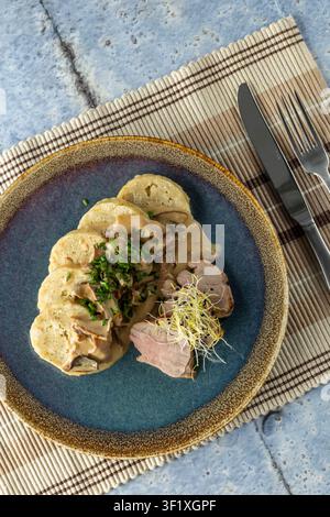 In Scheiben geschnittenes Schweinefilet mit cremiger Pilzsauce, Brotknochen und Sprossen auf einem Teller Stockfoto