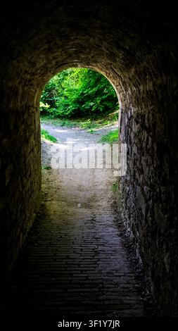 Historischer Festungstunnel, der sich zu einem sonnenbeschienenen Waldweg öffnet Stockfoto