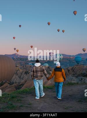 Wenn die Sonne über Kappadokien untergeht, schlendert ein Paar Hand in Hand, umgeben von farbenfrohen Heißluftballonen, die sanft über den einzigartigen Felsformationen dieser bezaubernden Landschaft schweben. Stockfoto