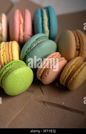 Nahaufnahme von pastellfarbenen französischen Macarons, die auf einer Kraftpapierbox gruppiert sind, Minze, Limette, Pfirsich, Türkis, Gelb und Beige Schalen mit cremiger Füllung, weich Stockfoto