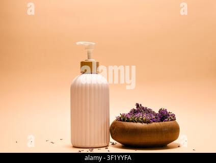 Eine moderne weiße Pumpflasche mit einem naturholzfarbenen Deckel ist elegant gepaart mit einer einfachen Holzschale voller Lavendelbeeren Stockfoto
