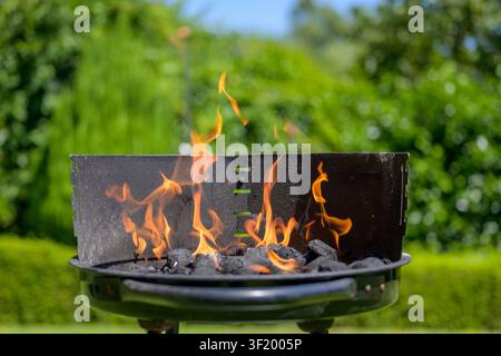 Helle orangefarbene Flammen tanzen über glühender Kohle in einem Barbecue-Grill an einem sonnigen Sommertag im Garten. Stockfoto