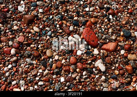 Nahaufnahme von bunten nassen Kieselsteinen und kleinen Steinen an einem Strand, die natürliche Textur, gemischte Formen und erdige Töne für den Hintergrund oder Naturdesign zeigen Stockfoto