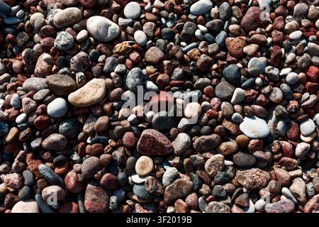 Nahaufnahme von bunten Mischpebbeln an einem felsigen Strand, die natürliche Steintexturen, abgerundete Formen und erdige Töne in einem einfachen Vollbild-Hintergrund zeigen Stockfoto