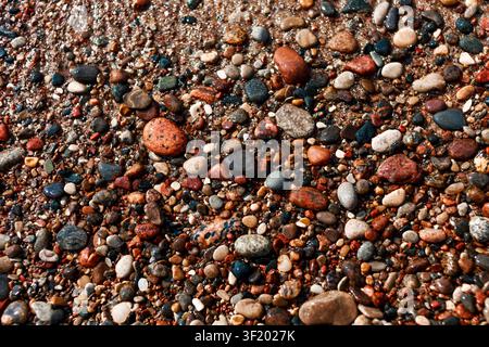 Nahaufnahme von bunten nassen Kieselsteinen und kleinen Steinen an einem Strand, die natürliche Textur, gemischte Formen und erdige Töne für den Hintergrund oder Naturdesign zeigen Stockfoto