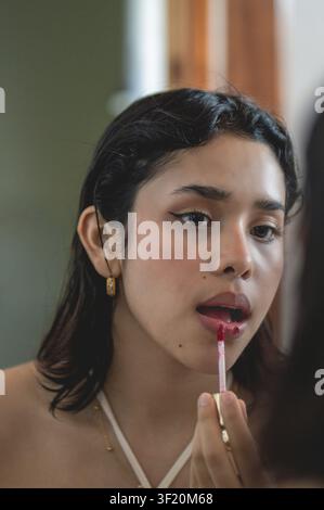 Junge Frau trägt roten Lipgloss auf, während sie in einen Spiegel schaut. Frau trägt Lippenstift während ihrer Schönheitsroutine auf Stockfoto