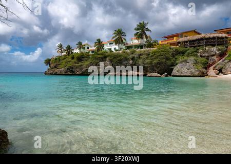 Das schöne kristallklare Wasser des Strandes Bahia Lagun in Curaçao zeigt eine felsige Bucht, die von tropischen Villen und Palmen gesäumt ist. Stockfoto