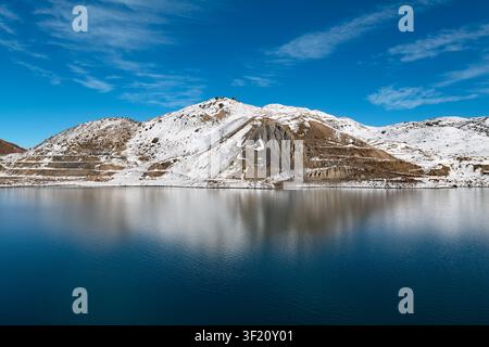 Wunderschöne malerische Aussicht auf den Embalse del Yeso-Stausee im Cajon del Maipo in Chile mit schneebedeckten Bergen, die sich auf der ruhigen blauen Wasseroberfläche spiegeln. Stockfoto