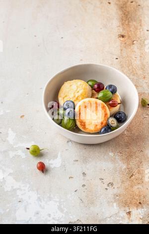 Hüttenkäse-Pfannkuchen Syrniki, Ricotta-Fritters mit frischen Beeren zum Frühstück auf beigem Holzgrund Stockfoto