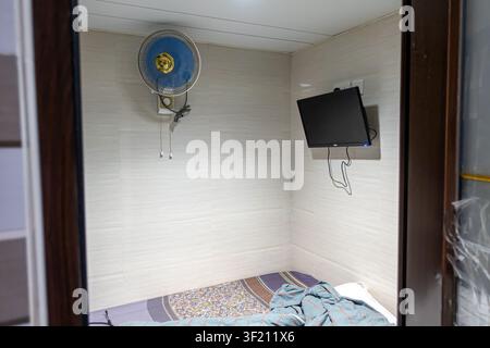 Kompaktes Hotelzimmer in einem Gästehaus in Hongkong, in den Chungking Mansions, mit gefliesten Wänden, einem kleinen Bett und einem wandmontierten Fernseher. Stockfoto