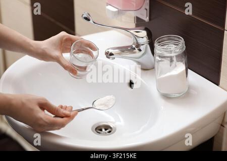 Eine Frau, die Backpulver benutzt, um den Abfluss im Bad zu reinigen, zu schließen Stockfoto