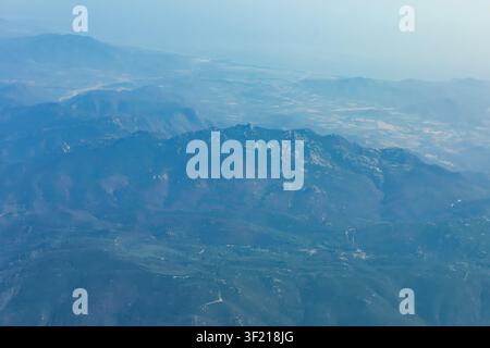 Luftaufnahme zeigt sich hügelige Bergketten, die sich unter sanftem blauem Dunst in die Ferne erstrecken. Das raue Gelände zeigt sich mit gewundenen Straßen Stockfoto