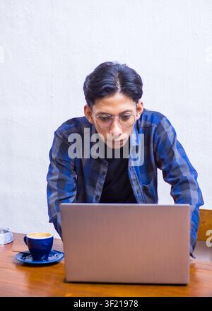 Konzentrierter junger Asiate, der sich auf seinen Laptop konzentriert, während er aus der Ferne in einem Café arbeitet, Lifestyle-Porträt. Stockfoto