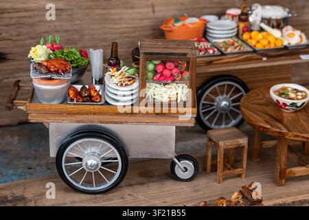 Chiang Mai, Thailand - 27. Mai 2026: Ein Miniaturmodell von einem Paprika-Salat-Wagen mit winzigem gegrilltem Huhn und Gemüse auf einem Bastmarkt Stockfoto