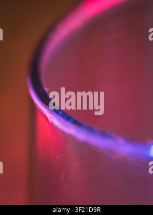 Makroabstraktfotografie eines Glasrandes, der von lebhaftem blauem und rotem Neonlicht beleuchtet wird und einen stimmungsvollen Gradienteneffekt erzeugt Stockfoto