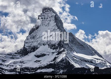 Blick auf den ikonischen Gipfel des Matterhorns mit seiner schneebedeckten Pyramidenform, der sich gegen einen hellblauen Himmel mit vereinzelten weißen Wolken in Zermatt erhebt Stockfoto