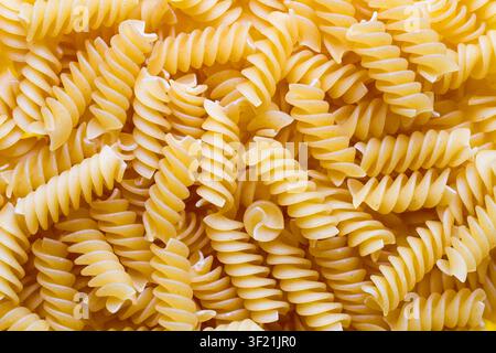 Rohe trockene Nudeln in Spiralform. Die Hintergrundtextur besteht aus vielen Nudelspiralen. Stockfoto