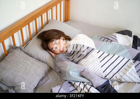 Indonesische Frau ruht im Bett, zugedeckt mit einer Decke, friedlicher Schlaf und gesunder Lebensstil im Innenraum. Stockfoto