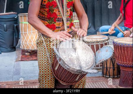 Musiker spielt Djembé-Hands Schlagzeug bei einer afrikanischen Trommelvorführung mit farbenfrohem traditionellem Kleid Stockfoto