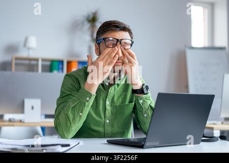 Konzentrierter kaukasischer Mann arbeitet am Schreibtisch, reibt sich die Augen im Büro, müde und gestresst, Geschäftskonzept Stockfoto