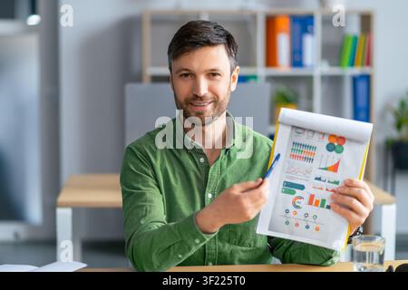 Lächelnder kaukasischer Mann präsentiert Geschäftsgrafiken und -diagramme im Büro, Geschäftskonzept Stockfoto
