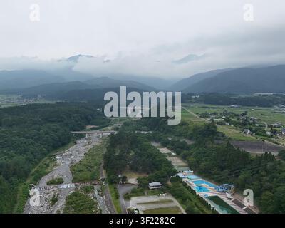 Bewölkter Himmel schwebt über sanft geschwungenen grünen Hügeln. Das Flussbett windet sich durch den bewaldeten Talboden. Felder und Bauernteiche erstrecken sich unter nebligen Gipfeln. Klein Stockfoto