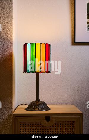Nahaufnahme einer kleinen, mehrfarbigen Tischlampe, die auf einem Stück Wohnzimmermöbel ruht. Bunte Beleuchtung und eine gemütliche Atmosphäre. Stockfoto