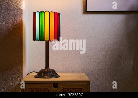 Nahaufnahme einer kleinen, mehrfarbigen Tischlampe, die auf einem Stück Wohnzimmermöbel ruht. Bunte Beleuchtung und eine gemütliche Atmosphäre. Stockfoto