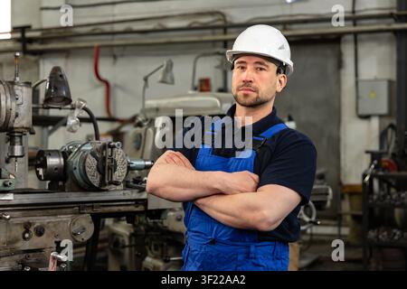 Selbstbewusster Industrieingenieur steht mit verschränkten Armen in der Fertigungswerkstatt Stockfoto