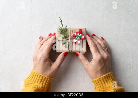 Hände, die ein handgemachtes Weihnachtsgeschenk mit Kraftpapier und Tannenast halten Stockfoto