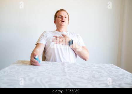 Mann, der an einem Asthmaanfall leidet, hält sich die Brust und hält ein Inhalationsgerät in der Hand Stockfoto