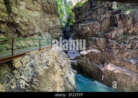 Ein schmaler Wanderweg mit einem grünen Geländer ist in die steilen Felswände der Breitachklamm in Bayern geschlagen. Unten ein lebendiger türkiser Fluss Stockfoto
