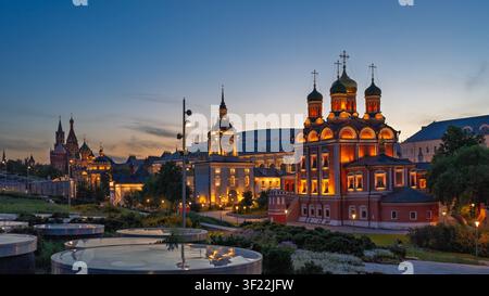 Beleuchtete orthodoxe Kirche im Zaryadye-Park in Moskau bei Dämmerung mit der Basilius-Kathedrale im Hintergrund. Historische Architektur und Abendlichter. Stockfoto