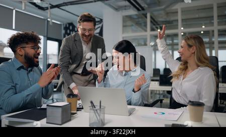 Vier multikulturelle Geschäftsleute gewinnen bei einem Meeting mit Laptop, feiern Erfolg, geben sich ein High Five, arbeiten, reden, glücklich, Team, Konferenzbesprechung Stockfoto