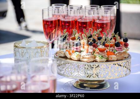 Elegante Außencatering-Ausstattung auf einer weißen Tischdecke, mit vorgefüllten Getränken und kleinen Häppchen, bereit für eine Feier Stockfoto