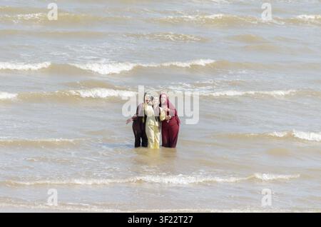 drei Freunde in ihrer traditionellen Kleidung stehen im Meer und machen ein Selfie in Clacton-on-Sea, Essex, UK Stockfoto