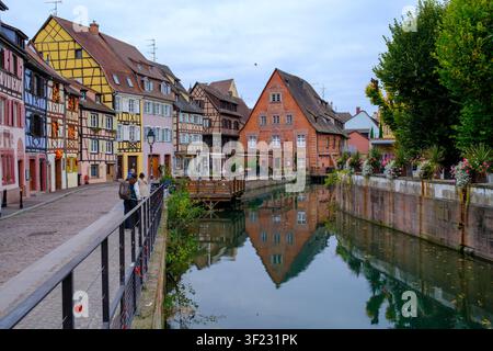 Colmar, Frankreich - 09. Juli 2026: Blick auf die historischen Fachwerkhäuser entlang des Kanals in La Petite Venise mit Menschen, die auf dem Kopfsteinpflaster spazieren Stockfoto